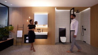 Un uomo e una donna in un bagno armoniosamente illuminato con mobili da bagno e ceramiche Geberit ONE (© Geberit)