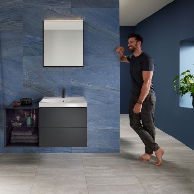 Uomo appoggiato alla parete in un bagno blu con lavabo Geberit Mix & Match