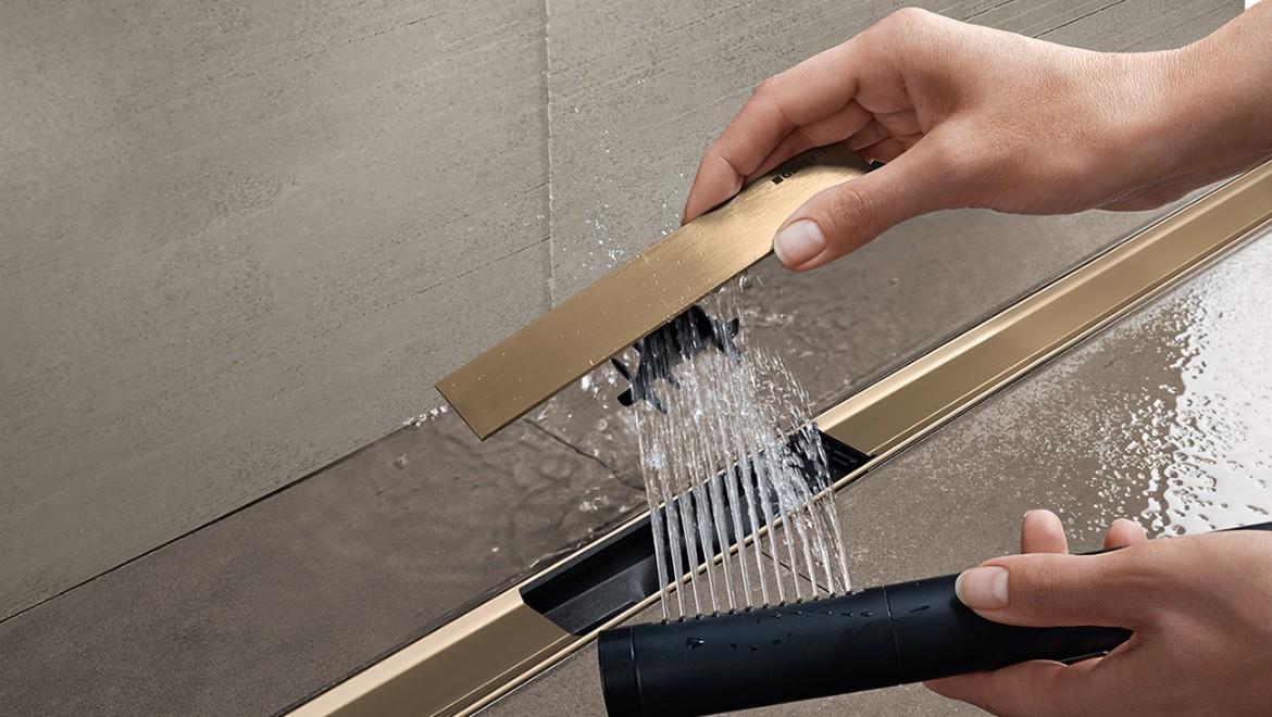 Femme retirant le filtre à cheveux de lʼécoulement de douche Geberit CleanLine pour le nettoyer (© Geberit)