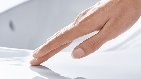 Hand streicht über Waschtischkeramik mit KeraTect Beschichtung Hand streicht über Waschtischkeramik mit KeraTect Beschichtung