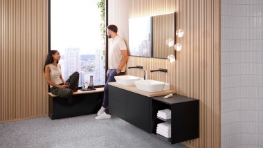 Femme assise sur le rebord d’une fenêtre parlant à un homme dans une salle de bains Geberit ONE