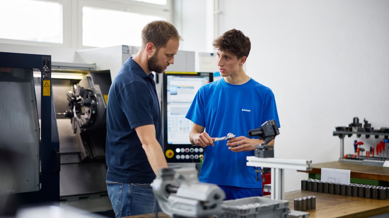Un apprenti chez Geberit suit une initiation dans l'atelier avec son formateur Un apprenti chez Geberit suit une initiation dans l'atelier avec son formateur